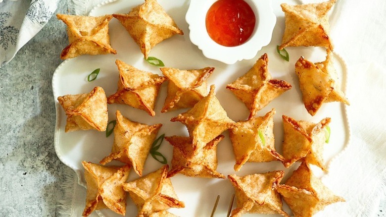 Crab rangoon on serving platter with small bowl of sweet chili dip