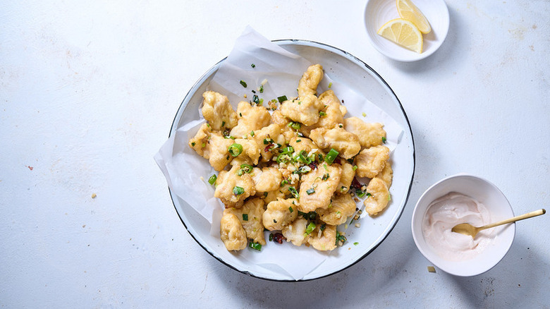Salt and pepper fried catfish in parchment-lined bowl next to small bowl of creamy dip