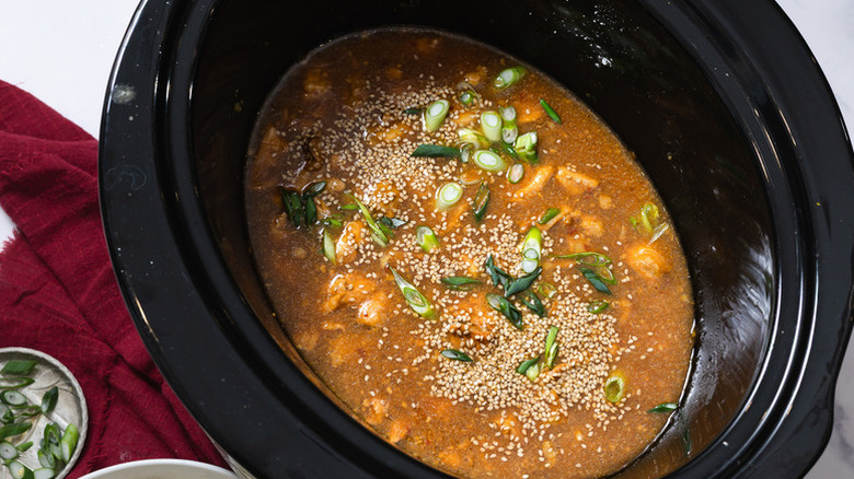 Orange chicken in slow cooker with chopped scallions and sesame seeds