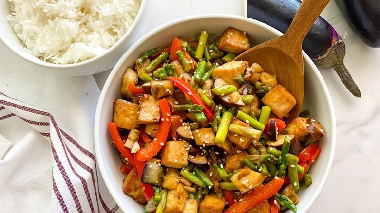 Eggplant, red pepper, and asparagus stir fry in bowl with wooden spoon