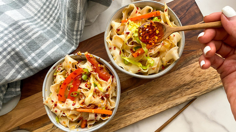 Spooning chili crisp onto bowls of garlic Szechuan noodles