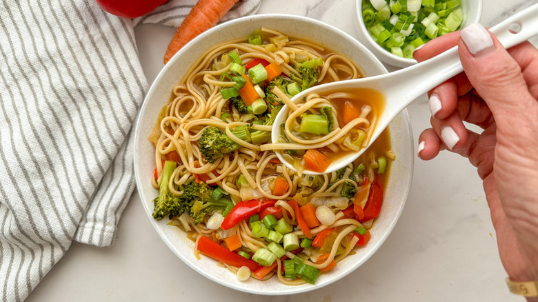 Spooning vegetable chow mein noodle soup from bowl