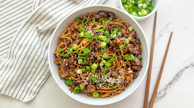 Bowl of mushroom dan dan noodles, garnished with chopped green onion and sesame seeds
