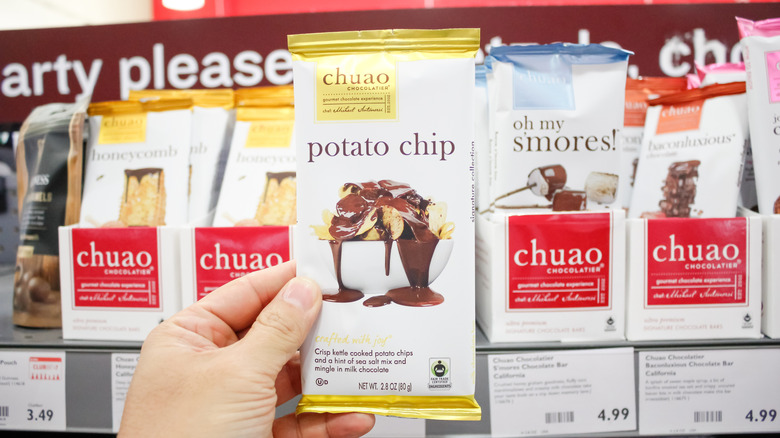 Hand holding a Chuao potato chip bar in a grocery store alongside other flavors