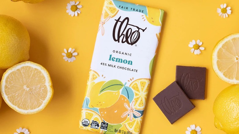 Lemon milk chocolate bar surrounded by fresh lemons, flowers, and two squares of chocolate