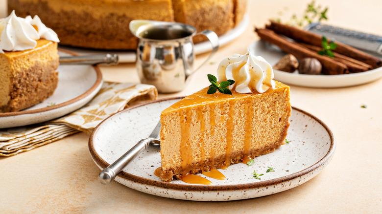Slice of pumpkin cheesecake on a plate, topped with a swirl of whipped cream