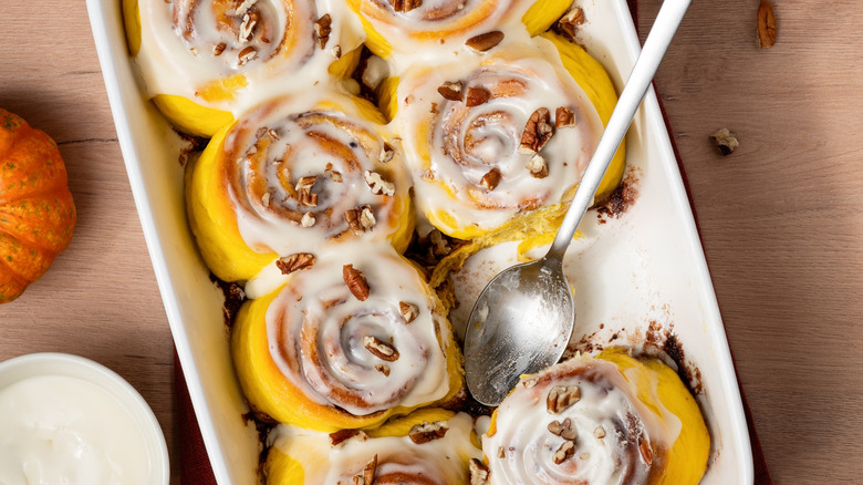 Pumpkin cinnamon rolls in a white baking dish with a spoon