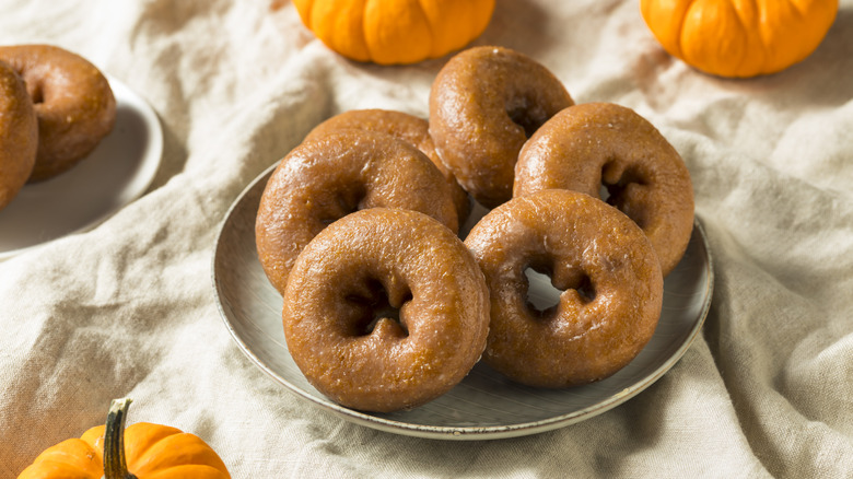Pile of pumpkin donuts on a plate, next to fresh pumpkins