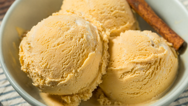 Three scoops of pumpkin ice cream in a bowl with a cinnamon stick