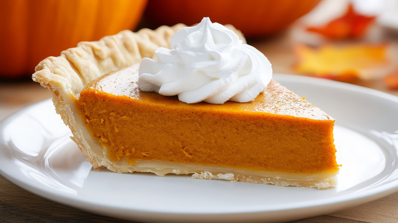 Slice of pumpkin pie on a plate, topped with a swirl of whipped cream
