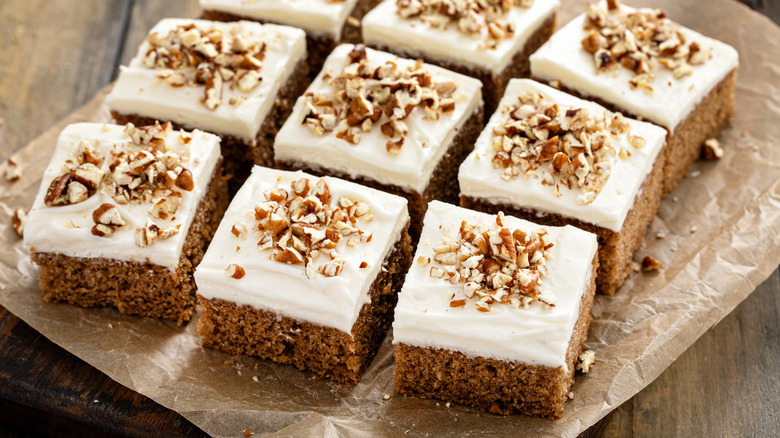 Squares of pumpkin sheet cake on a piece of parchment paper, topped with frosting and chopped nuts