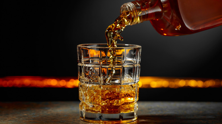 A bottle of Scotch being poured into a glass.