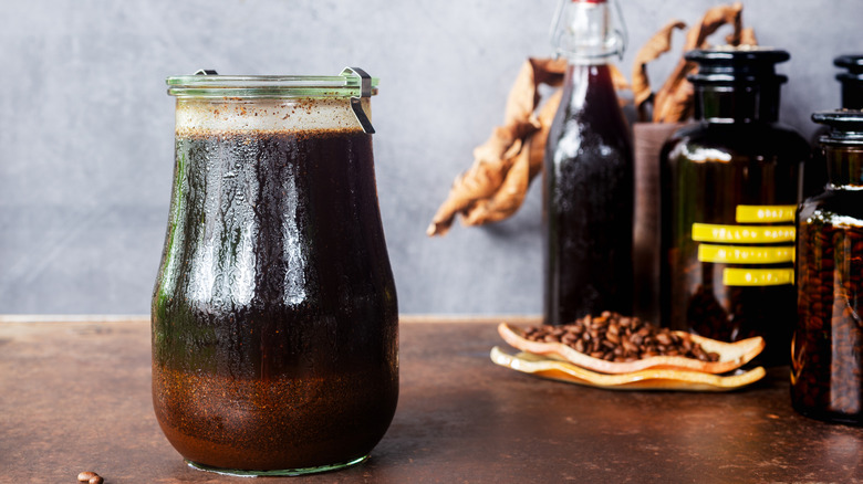 Jar of homemade cold brew sitting on counter, other coffee beans and accessories behind