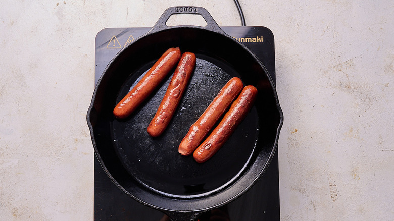 Aerial view of four hot dogs cooking in a skillet
