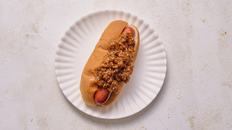 A single hot dog in a hot dog bun topped with Coney sauce on a plate