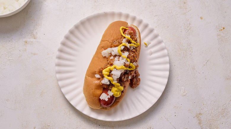 One Coney Island hot dog topped with mustard and onions on a plate