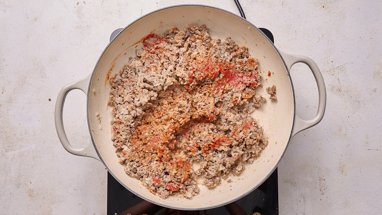 Aerial view of tomato paste stirred into ground beef in pot