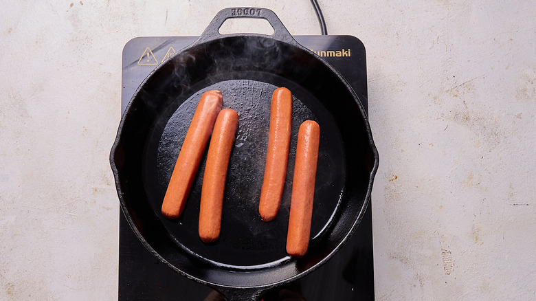 Aerial view of four hot dogs cooking in pan