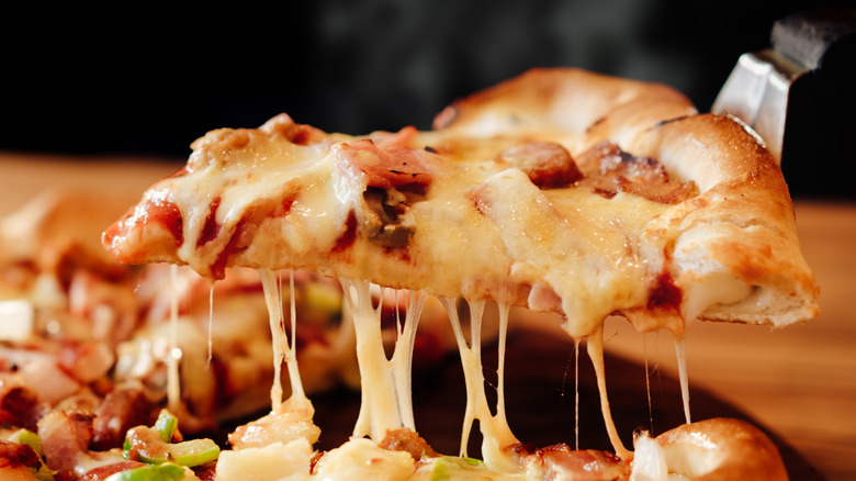 Lifting a slice of cheesy pizza from a pizza pie