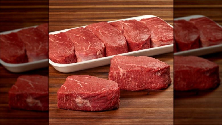 Kirkland Signature Prime Beef Loin Top Sirloin Steaks in white tray next to two steaks on wooden surface