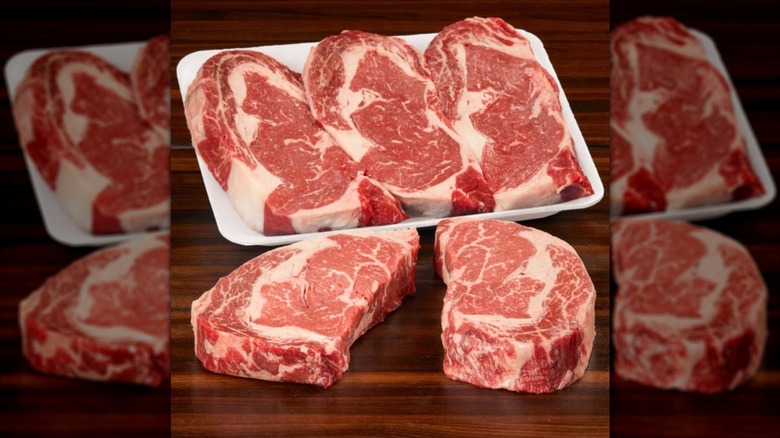 Raw Kirkland Signature Prime Boneless Ribeye steaks in white tray next to two more steaks on wooden surface