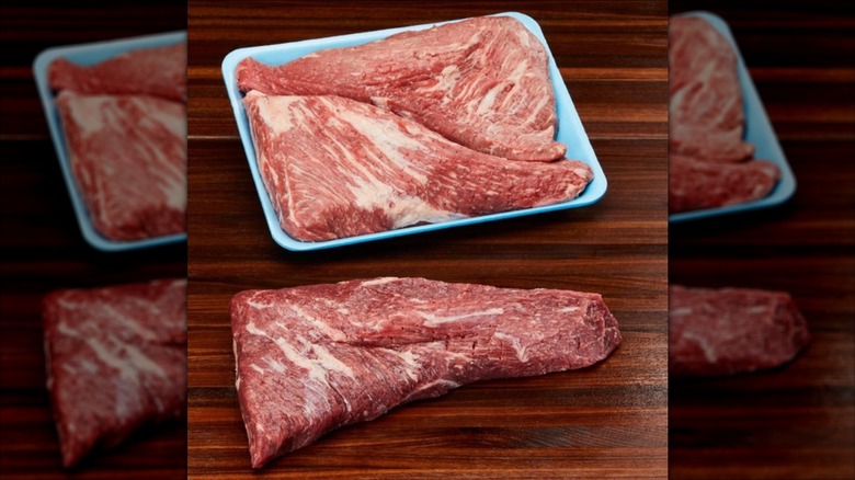 Two Kirkland Signature Prime Beef Loin Tri Tip steaks in blue tray next to third steak sitting on wooden table