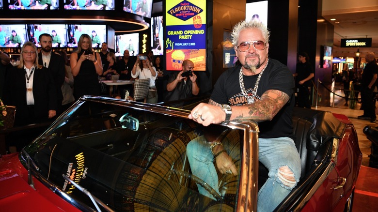 Guy Fieri posing with his red car from "Diners, Drive-Ins and Dives" at an event