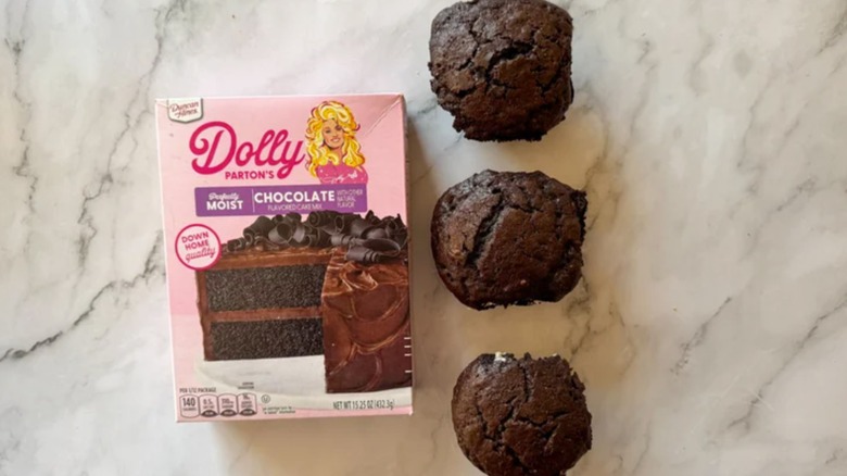 Dolly Parton's boxed chocolate cake mix on a counter next to three cupcakes