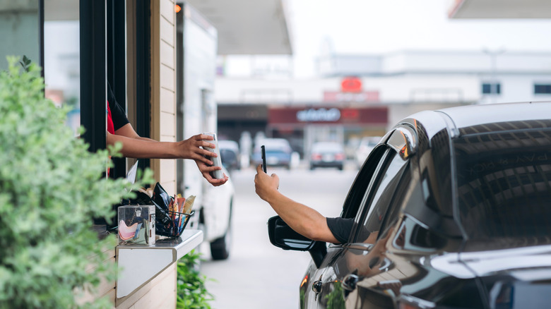 A person in a car using a phone to pay at a drive-thru
