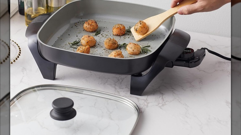A person flipping food in an Elite Gourmet electric skillet