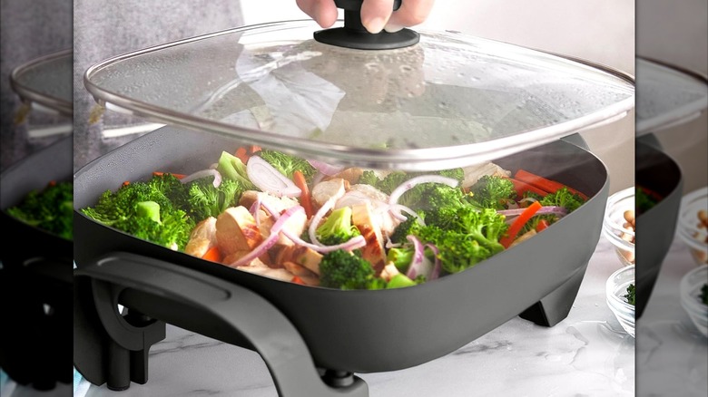 A person taking the lid off of an electric skillet