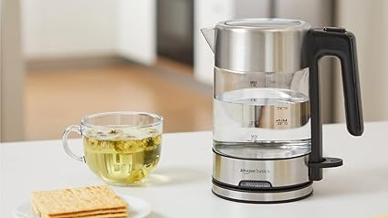 Amazon Basics tea kettle with a cup of hot tea on a white countertop