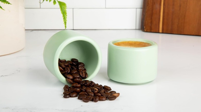 Two Folk Ceramics espresso cups on a countertop, with one tipped over spilling coffee beans and the other full of coffee