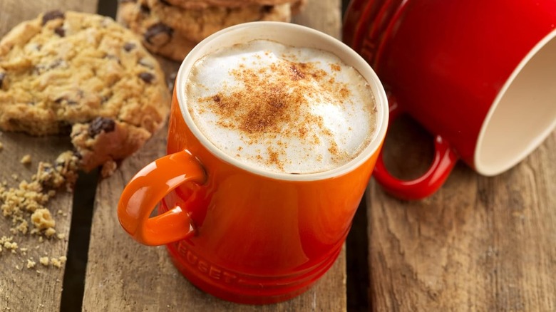 Close-up of a Le Creuset mug on a bench, next to a couple of cookies and another mug on its side
