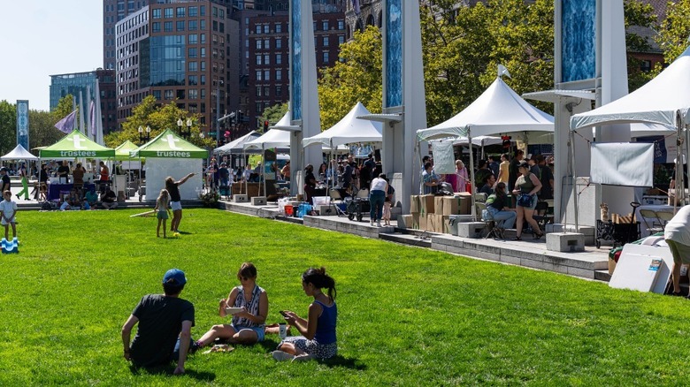 People sitting on the grass with tents in the background at the Boston Local Food Festival