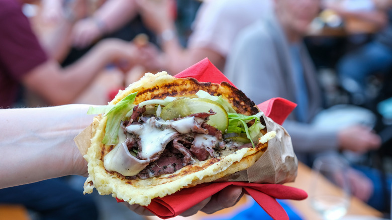 Hand holding a pastrami sandwich at a food festival