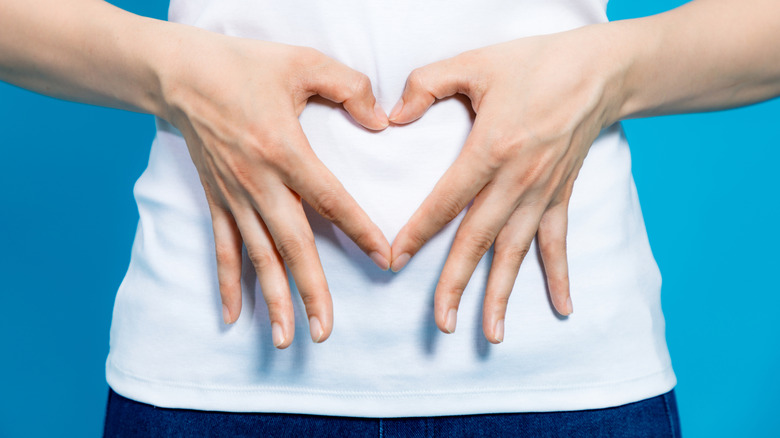 Woman in a white shirt making heart hands over her abdomen