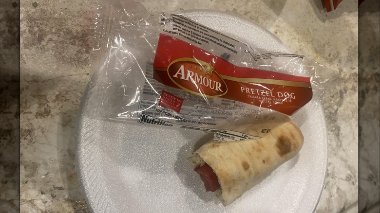 An Armour pretzel dog on a paper plate next to the empty wrapper
