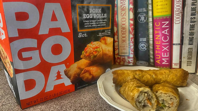 A box of Pagoda brand egg rolls sitting in front of some cookbooks with a plate of cooked egg rolls next to it