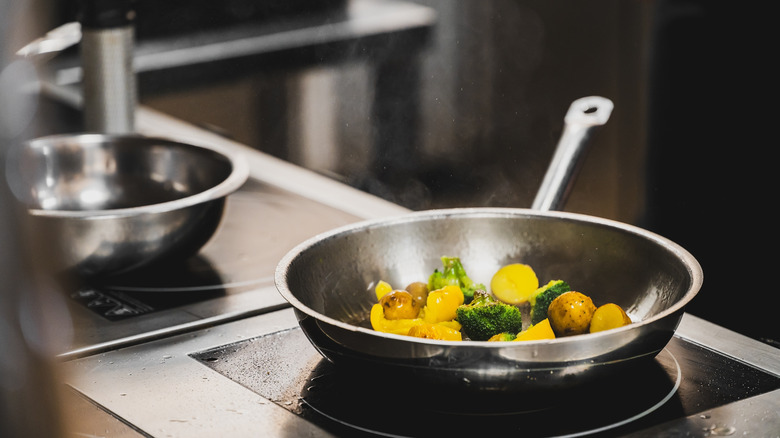 stainless steel frying pan with veggies and potatoes on stove