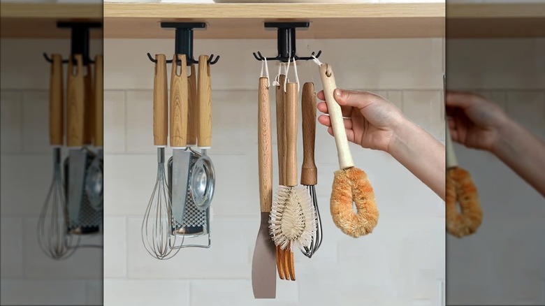 A person removing a brush from a DEPAOTLUX under-cabinet kitchen utensil hook