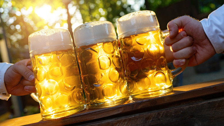 Two people holding three mugs of beer at a table