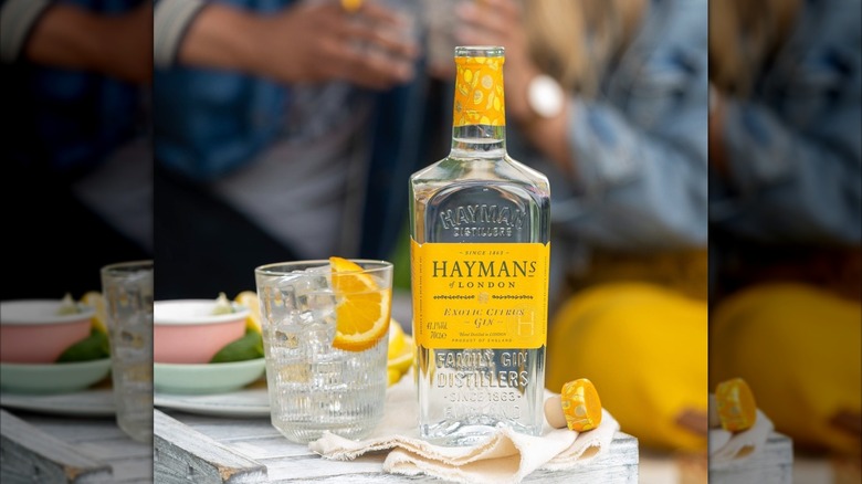 Bottle of Hayman's Exotic Citrus Gin next to a G&T with people blurred in the background
