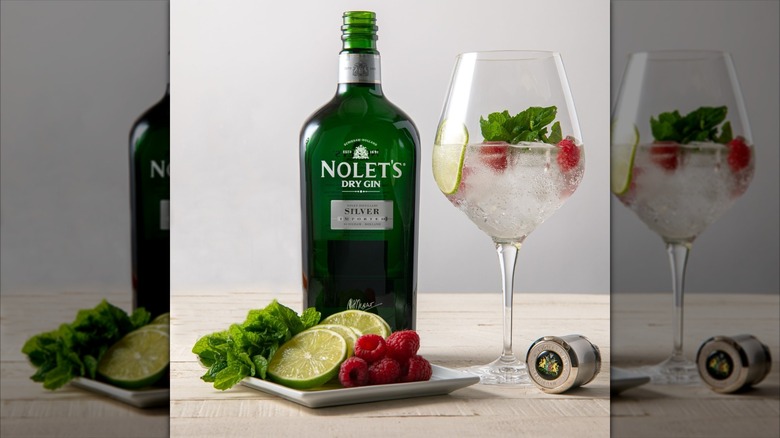 Bottle of Nolet's Silver Gin next to a gin and tonic and garnishes