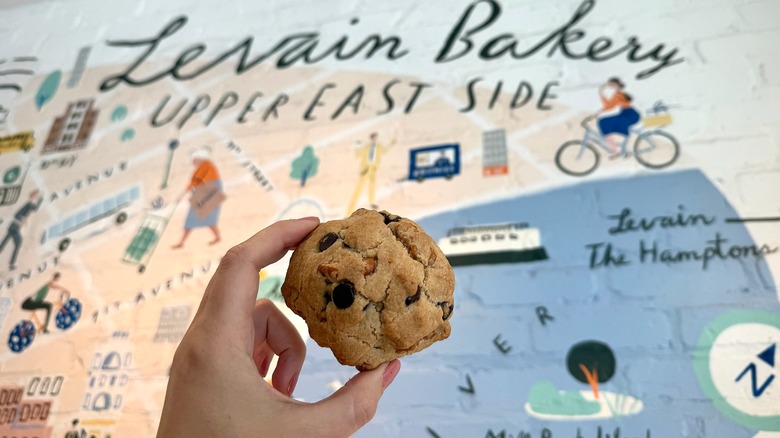 Levain cookie being held up against a graphic wall at Levain Bakery