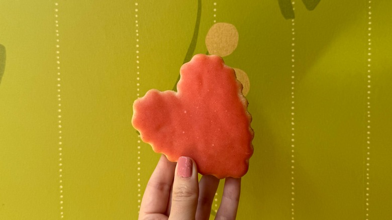 heart shaped cookie held up against green wall