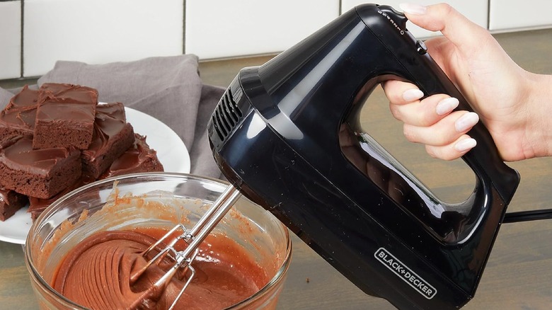 A person using a BLACK+DECKER hand mixer