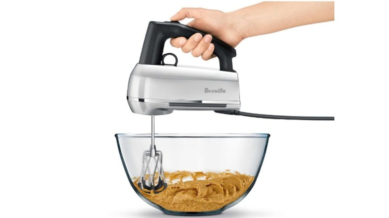 A person holding a Breville hand mixer in a mixing bowl
