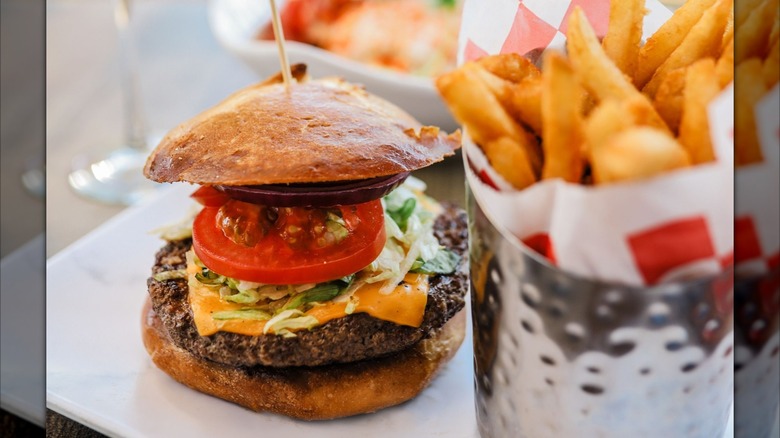 Burger with fries in a silver container on white plate