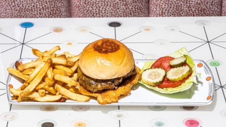 Burger on a plate with fries, tomatoes, picke, and lettuce all on the side
